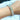 A stretchable bikini jewelry bracelet with a silver tone, featuring a series of round crystal rhinestones in a rainbow color on a person's wrist.