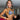 A pair of long, chandelier-style bikini jewelry earrings with clear crystal rhinestones mounted on a silver-colored frame, displayed by an npc bikini fit model.