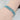 A stretchable rhinestone bikini jewelry bracelet with clear and teal stones on a silver metal base, displayed on a person's hand.
