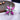 A silver-colored stretch cocktail bikini jewelry ring with a flower design accentuated by clear and pink rhinestones, displayed on a wooden surface.